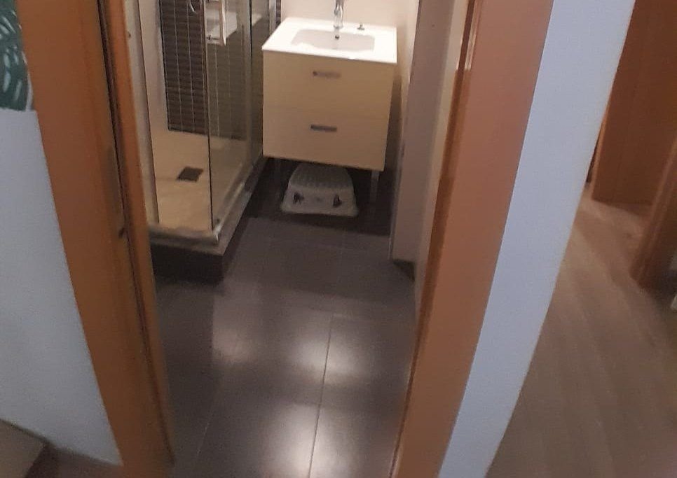 Baño reformado: plato de ducha con mampara, mueble de lavabo blanco y suelo gris