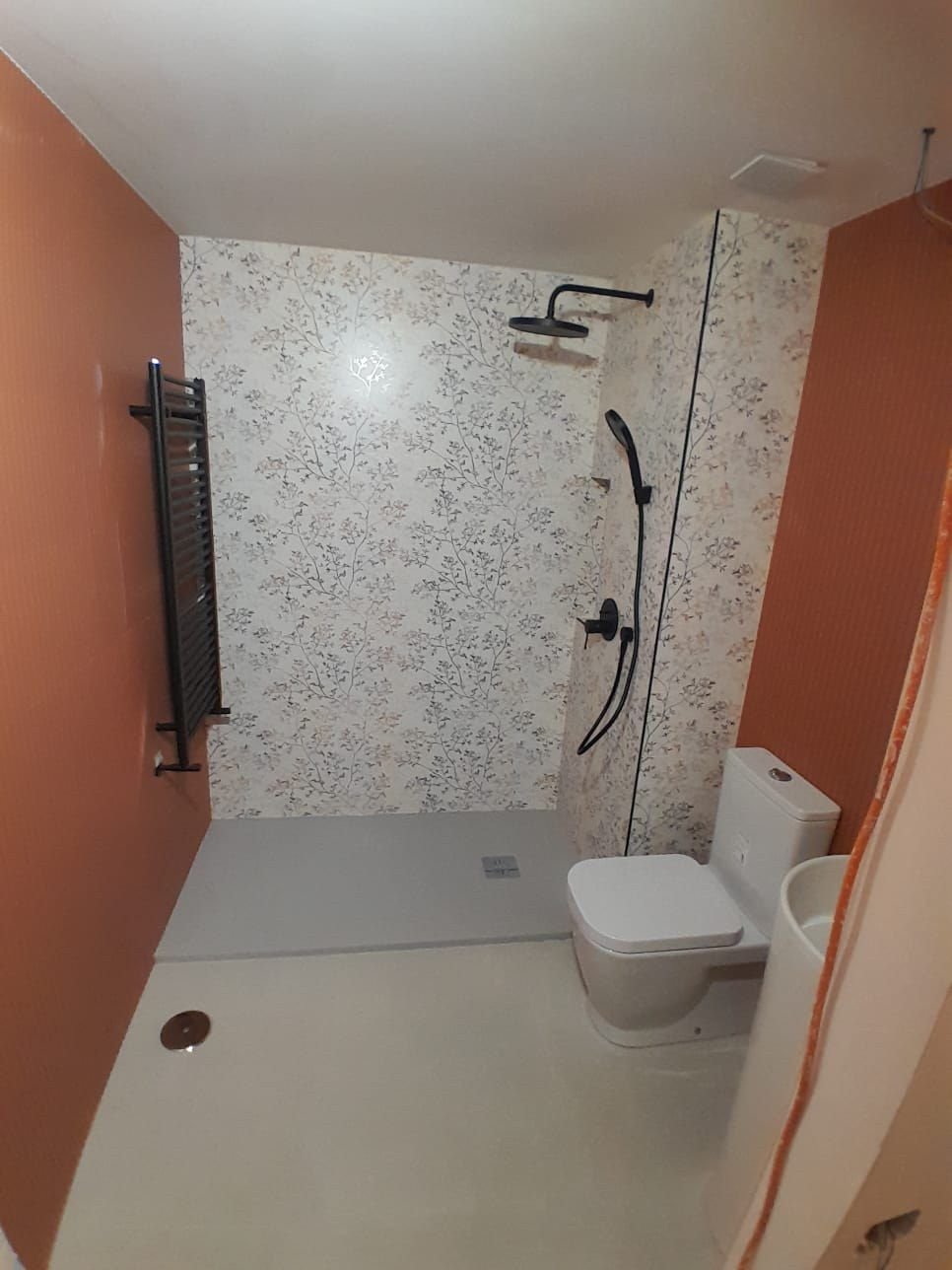 Baño terminado con pared de azulejo acanalado terracota, papel floral y grifería negra